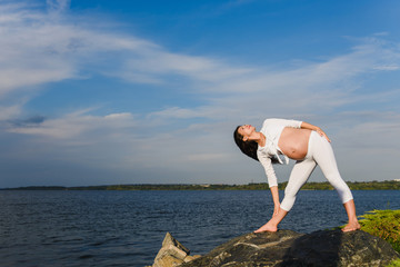 Pregnant woman is practicing yoga beside river