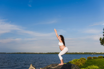 Pregnant woman is practicing yoga beside river