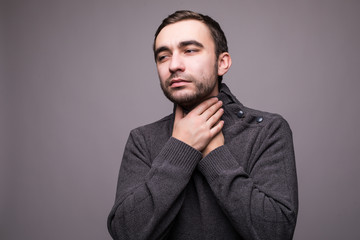 Young man having sore throat and touching his neck against light grey background.