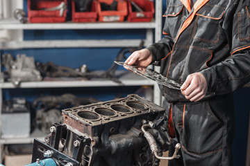 Naklejka premium Sealing gasket in hand. The mechanic disassemble block engine vehicle. Engine on a repair stand with piston and connecting rod of automotive technology. Interior of a car repair shop.