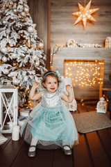 Pretty little girl in blue dress looks funny posing in cosy room decorated for winter holidays