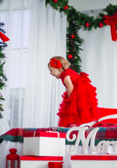 Obraz premium Pretty little girl in red dress looks funny posing in cosy room decorated for winter holidays