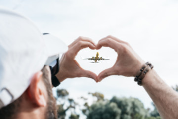 Man showing a heart sign with a plane flying in the middle