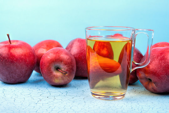 Glass of apple juice and red apples on wooden background .