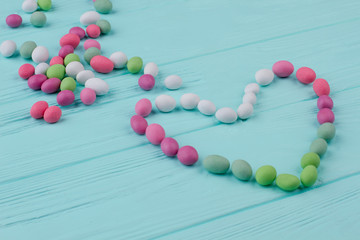 Group of round candies on wooden background. Heart made from many vibrant multicolored candies. Saint Valentines Day.