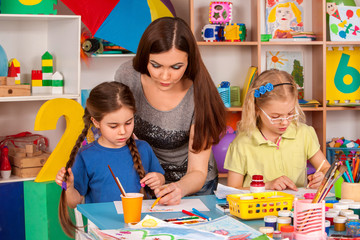 Fototapeta premium Kids playroom organization of children painting and drawing in kid's club. Craft lesson in primary school. Kindergarten teacher and small students work together. Girl paints felt-tip pen. Children
