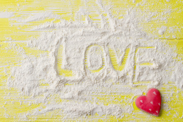 Word love written on sugar powder. Red heart shaped cookie on yellow wooden background in corner. Happy Valentines Day.