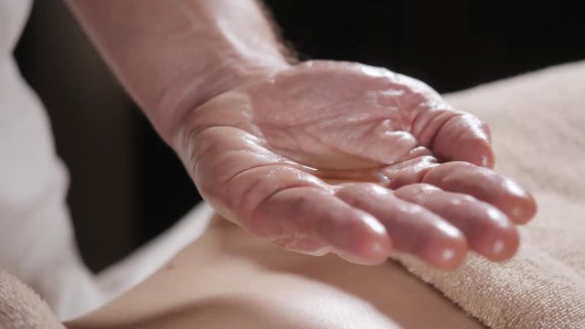 close-up pours oil in the palm. Osteopath doing manipulative massage on female abdomen. Man hands massaging female.Therapist applying pressure on belly. Spa centre concept