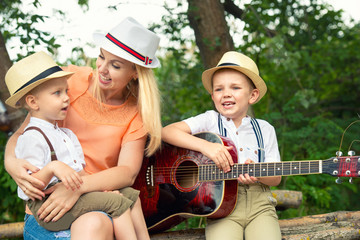 Young mother and two sons are resting in the woods,singing songs with a guitar.	