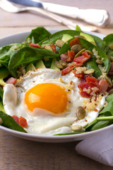 Fried egg with bacon, quinoa, avocado, spinach and pumpkin seeds for breakfast