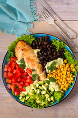 Chicken dish with nutritious selection of vegetables: avocado, beans, tomatoes and sweet corn. Chicken breast salad
