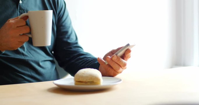 Man using mobile phone while having cup of coffee at home 