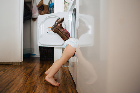 Toddler siblings playing in the dryer and hiding from mom.