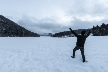 Victorious young man with arms raised to the sky in the middle of a snow-covered land in the mountains. Sense of peace, freedom, serenity, carefree, satisfaction, happiness . Cloudy day