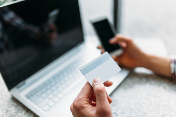 A man sits in a cafe with a laptop, make purchases via the online store, payment by credit card, a plastic card