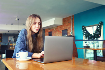 Woman working on laptop in a cafe. Young woman sitting at a table with a coffee usinglaptop. With blank copy space scree for your advertising text message or promotional content Toned image. Selective