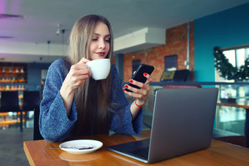 Woman typing text message on smart phone in a cafe. Young woman sitting at a table with a coffee using mobile phone. With blank copy space scree for your advertising text message or promotional