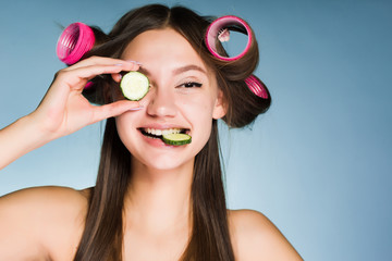 a funny young girl wants to look good, on the head of curlers, holds a cucumber for moisturizing...