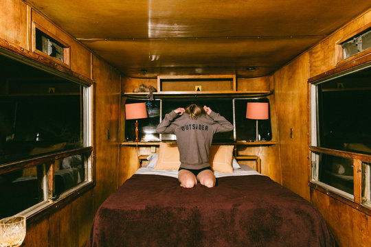 Woman Sitting On A Bed In a Trailer Taking Off Her Sweatshirt