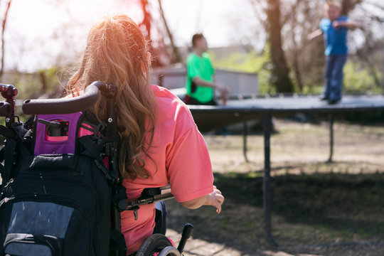 Girl In Wheelchair Watches Friends On Trampoline