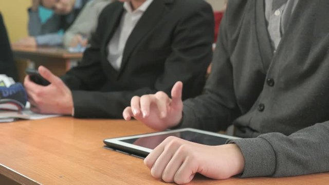 Two students sit at desk at office. One man holding smartphones other man looking at white-black computer tablet pressing them fingers on screen and look at important information