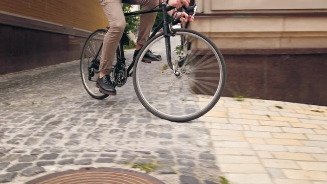 4k footage of stylish man riding black vintage bicycle om paved road of narrow street