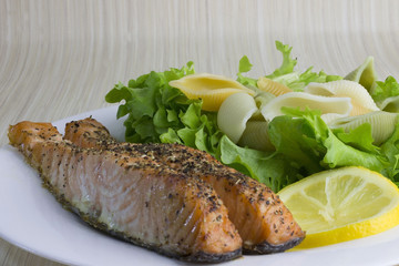 Fried salmon with shell-shaped pasta, salad and lemon on a plate