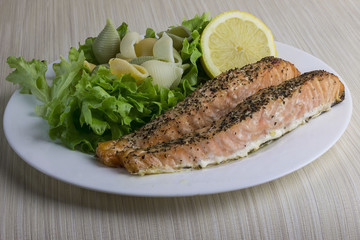 Fried salmon with shell-shaped pasta, salad and lemon on a plate