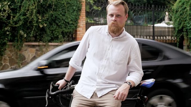 4k footage of stylish bearded man in white shirt leaning on bicycle on old street