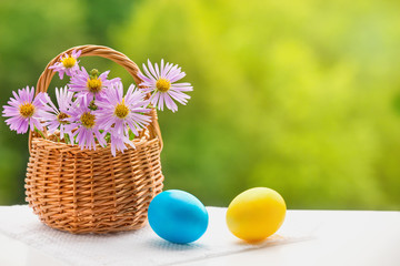 Two Easter eggs on white background and flowers in basket on green blurred background. Selective focus. Close up easter painted eggs. The Concept Of Easter. Side view, horizontal.