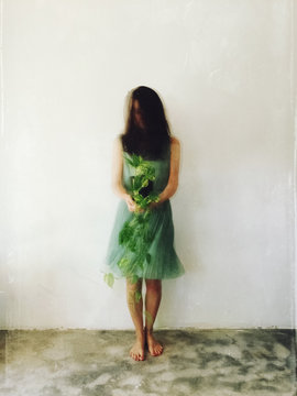 Movement shot of unrecognisable female wearing  green dress, holding Devil's Ivy plant