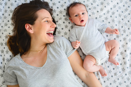 Mother playing with baby on bed.