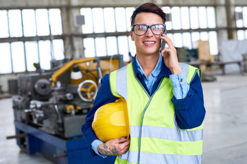 Portrait of modern female worker speaking by phone in workshop of industrial plant, copy space