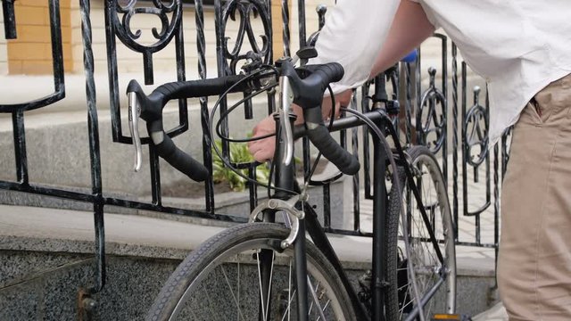 4k footage of young man locking his bicycle to fence with chain and combination lock
