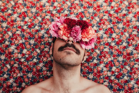 man wint flowers covering his eyes behind a foral bakground