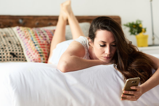 Pretty brunette girl using mobile phone  on bed.