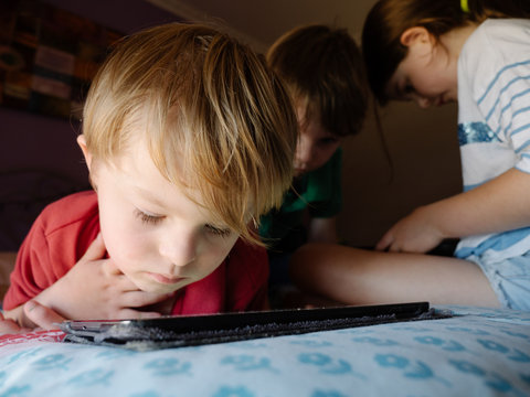 Preschool Boy Using Tablet with Brother and Sister in Background