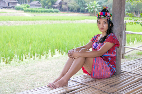 Asian woman in traditional costume for Karen resting beside green rice field