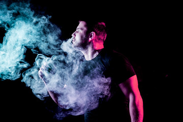 The man smoke an electronic cigarette on the dark background