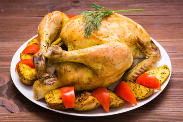 Baked whole chicken with a garnish of potatoes and tomatoes on a plate