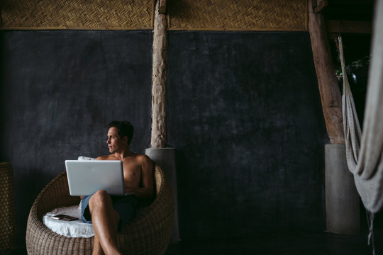 Man in his 30's working on laptop in chair on vacation