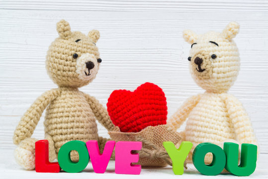 Sweet couple teddy bear doll in love with Love text and red knitting heart on white wooden background and copy space for add text and picture, love and valentine day concept.