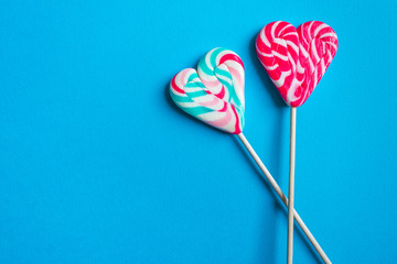Close up and top view of colorful heart shaped striped lollipops isolated on blue background with copy space, love or Valentine's day concept