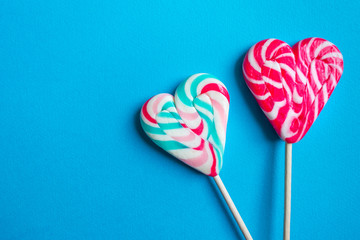Close up and top view of colorful heart shaped striped lollipops isolated on blue background with copy space, love or Valentine's day concept
