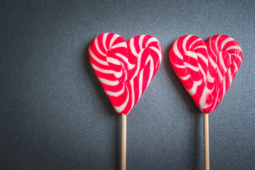 Close up and top view of two heart shaped red and white striped lollipops isolated on gray background with copy space, love or Valentine's day concept 