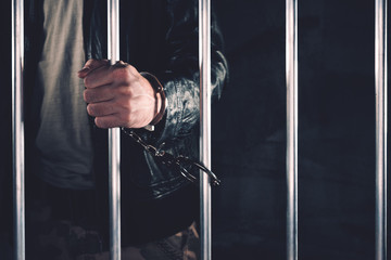 Fototapeta na wymiar Handcuffed man behind prison bars