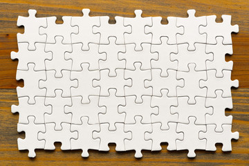 Puzzle background. White pieces on wooden table. Partially completed box shaped puzzle pieces.
 - obrazy, fototapety, plakaty