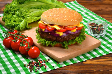 Delicious tasty burger with beef, tomatoes, salad and sauce on wooden table and black background. 