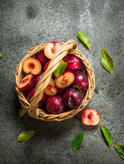 Fresh plums in a basket with leaves.