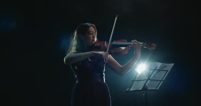 Violinist girl performing on stage, light, dark background
